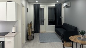 Un appartement moderne doté d’une kitchenette, d’un coin repas avec une table ronde et des chaises, d’un canapé noir et d’une grande fenêtre avec des rideaux.