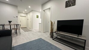 Un salon moderne doté d’un téléviseur à écran plat, d’un coin repas avec des chaises et une table, et d’un couloir menant à une porte.