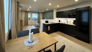 Une cuisine moderne avec un coin repas, comprenant une table en bois, des meubles de rangement noirs et un réfrigérateur noir.