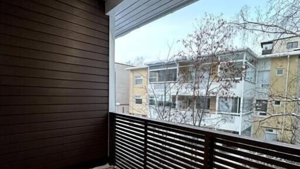 Un balcon doté d’un plancher en bois et de rampes en métal, qui offre une vue sur un quartier résidentiel avec ses immeubles et ses arbres sans feuilles.