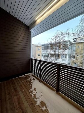 A balcony with wooden flooring and metal railings, overlooking a residential area with buildings and bare trees. - Kotimaailma Apartments (Seinäjoki)