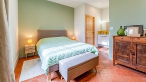 Une chambre à coucher comprenant un lit, une table de chevet, un banc, une armoire et une porte.
