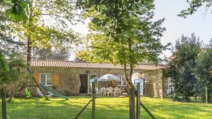 Ein Steinhaus mit Ziegeldach, einem Rasen, einer Schaukel und einer Terrasse mit Gartenmöbeln.