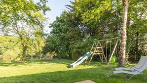 Ein Garten mit Schaukel, Rutsche und einer gefliesten Terrasse.