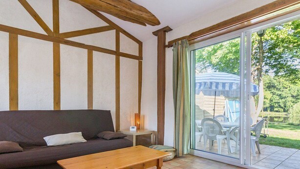 Ein Zimmer mit Holzboden, einer Couch, einem Tisch und einer Glastür, die zu einem Außenbereich mit Pool und Stühlen führt.