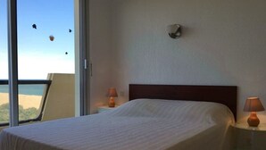 A bedroom with a large bed, two bedside tables with lamps, a window with a view of the beach, and a wall-mounted light fixture. - 3-room seafront apartment, terrace, pets allowed, parking (Argelès-sur-Mer)