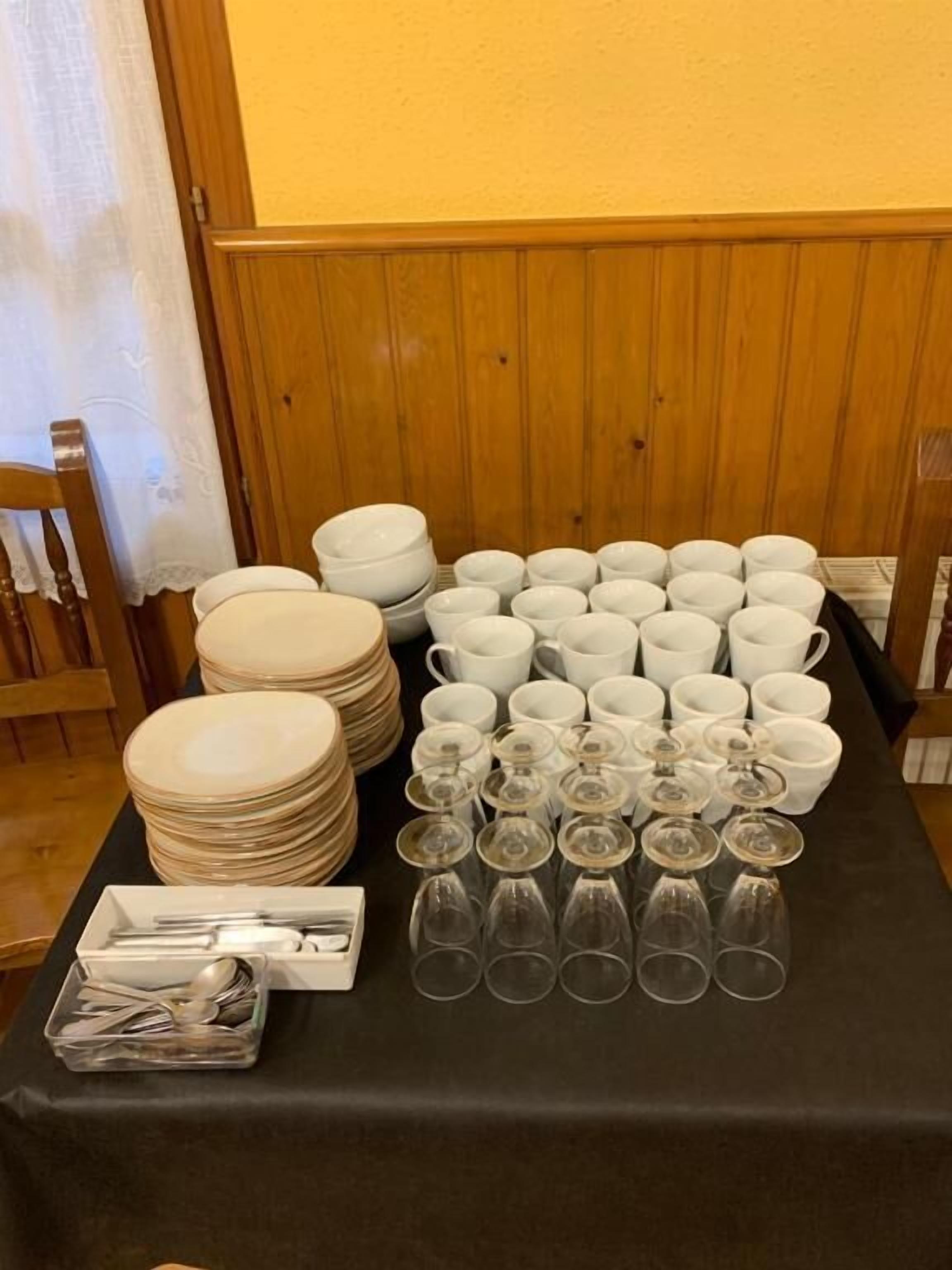 Una mesa dispuesta con platos, tazones, vasos y copas de vino, junto con cubiertos y un recipiente pequeño con salsas.
