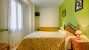 A bedroom with a bed, a nightstand, a lamp, and a wall-mounted TV. - Hostal Kimboa (Ansó)