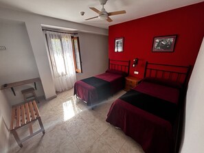 A bedroom with two beds, a ceiling fan, a window with curtains, and a small wooden bench. - Hostal Kimboa (Ansó)