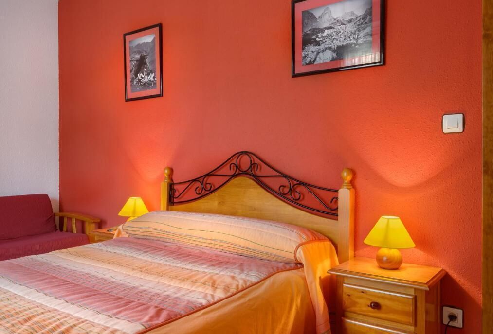 A bedroom with a wooden bed, two bedside lamps, and two framed pictures on the wall.