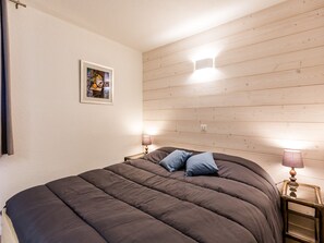 A bed with a dark-colored duvet and two pillows, a bedside table with a lamp, and a framed picture on the wall. - 2-room apartment near slopes - 5 people (La Plagne Montchavin Les Coches)