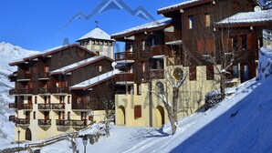 A multi-story hotel with balconies, a ski lift in the background, and snow-covered surroundings. - 2-room apartment near slopes - 5 people (La Plagne Montchavin Les Coches)