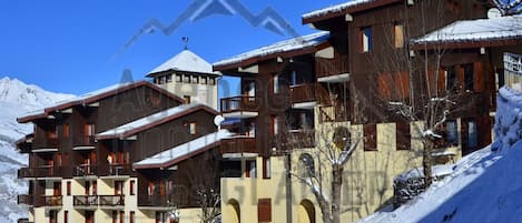 A multi-story hotel with balconies, a ski lift in the background, and snow-covered surroundings.