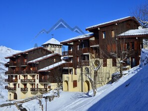 A multi-story hotel with balconies, a ski lift in the background, and snow-covered surroundings. - 2-room apartment near slopes - 5 people (La Plagne Montchavin Les Coches)