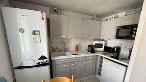 A compact kitchen with a refrigerator, microwave, sink, and a dining area with chairs. - Holiday home with pool, close to beach - La Tranche-sur-Mer (La Tranche-sur-Mer)