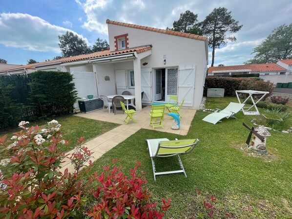 Une maison blanche avec un toit en tuiles, une terrasse avec des chaises vertes et un moulin à vent.