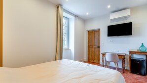 Una habitación de hotel con una cama, un escritorio, una silla, un televisor y un equipo de aire acondicionado.