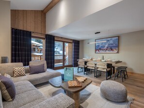 A modern living room with a sofa, ottoman, and coffee table, a dining area with chairs and a table, and a large window with curtains. - Appartement neuf au pied des pistes pour 9 personnes (Saint-Martin-de-Belleville)