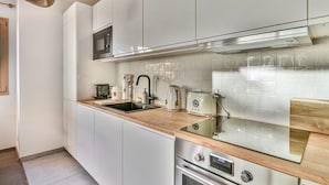 A modern kitchen with white cabinets, a stainless steel oven, a microwave, a sink, and a wooden countertop. - Charming T2 with cabin 50m from slopes for 4-5 pers (Les Gets)