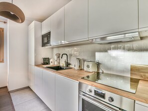 A modern kitchen with white cabinets, a stainless steel oven, a microwave, a sink, and a wooden countertop. - Charming T2 with cabin 50m from slopes for 4-5 pers (Les Gets)