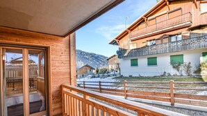 A wooden balcony with a view of a snow-covered village and mountains. - Charming T2 with cabin 50m from slopes for 4-5 pers (Les Gets)