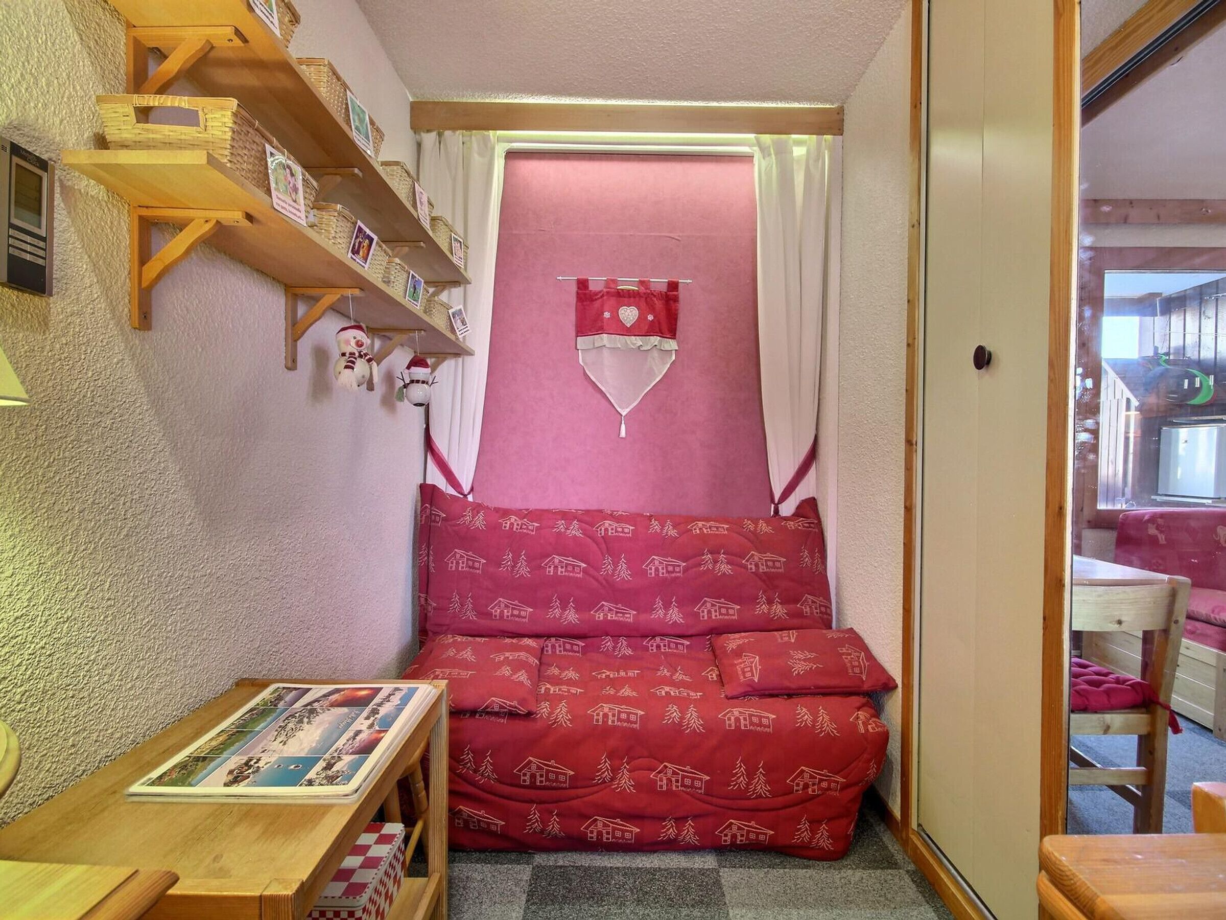 A cozy room with a red sofa, wooden shelves, and a small table with a book.