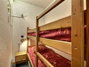 A small, compact room with bunk beds, a small wooden table, and a wall-mounted electrical outlet. - Central studio with balcony in Belle Plagne, 4 pers (Belle Plagne)
