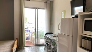 Un espacio habitable compacto con kitchenette, zona de comedor con mesa y sillas, banco de madera y puerta corrediza de vidrio que da a un área exterior.