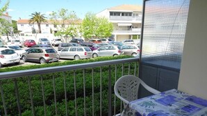 Un balcón con vista a un estacionamiento y edificios. Se ve una silla y una mesa con mantel.