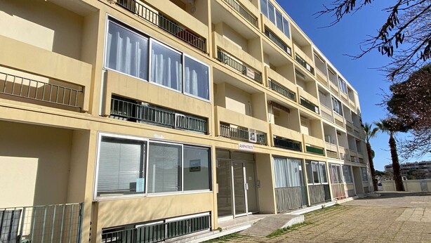Un edificio residencial de varios pisos con balcones, amplias ventanas y un área pavimentada en la planta baja.