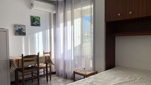 Ein Schlafzimmer mit Bett, einem kleinen Tisch, einem Stuhl, einem Schreibtisch und einem Fenster mit Vorhängen.