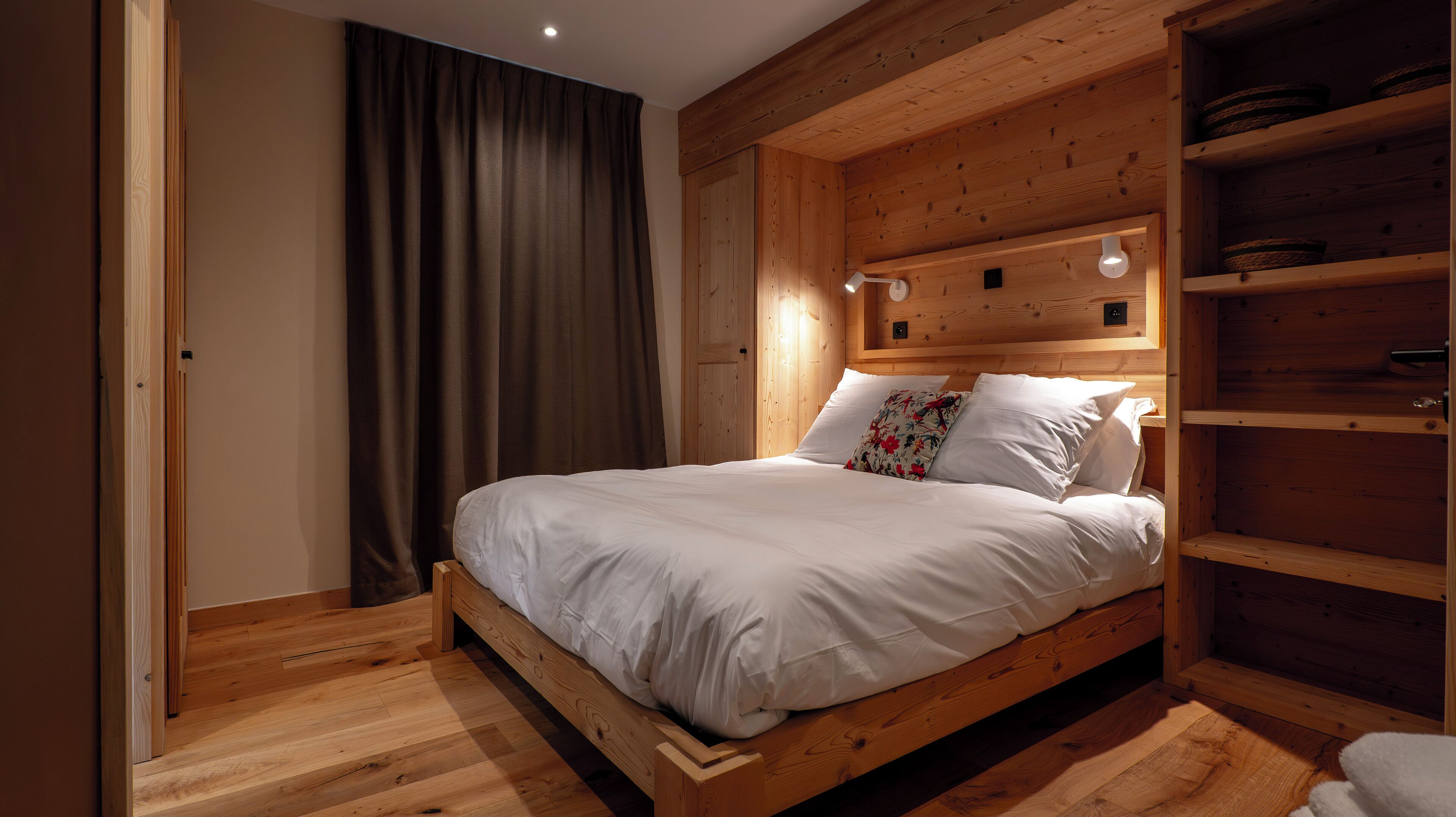 A wooden bed with white bedding, a wooden headboard with built-in lighting, and a wooden floor.