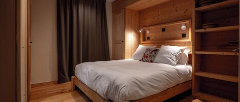 A wooden bed with white bedding, a wooden headboard with built-in lighting, and a wooden floor.