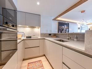 A modern kitchen with a built-in oven, a large sink, and a wooden ceiling beam. - Luxury apartment with fireplace, terrace, and relaxation access (Val-d'Isère)