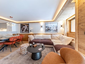 A modern living room with a dining area, wooden walls, and artwork. - Luxury apartment with fireplace, terrace, and relaxation access (Val-d'Isère)