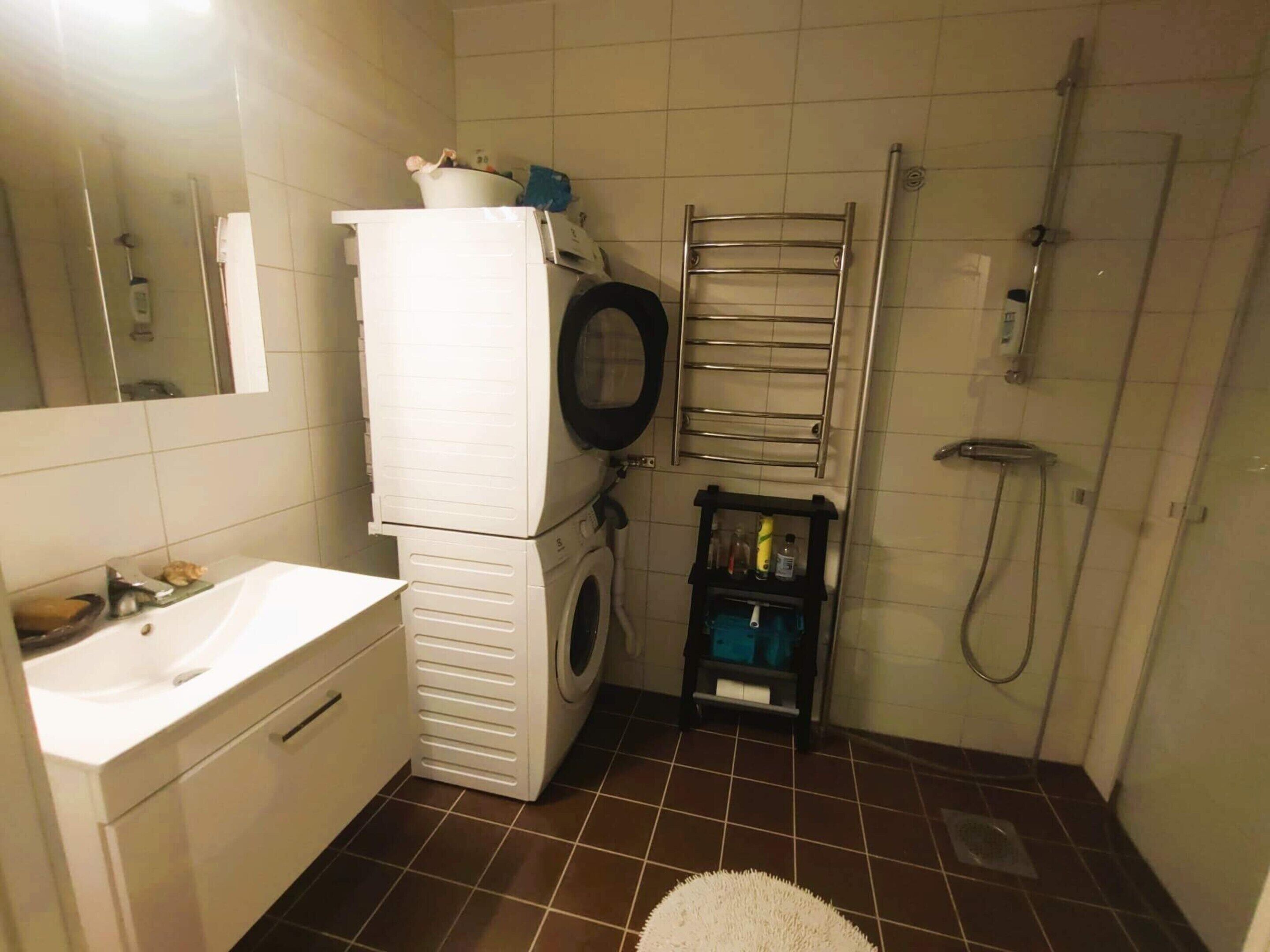 Un bagno compatto con lavandino, lavasciuga affiancata, porta asciugamani e doccia.