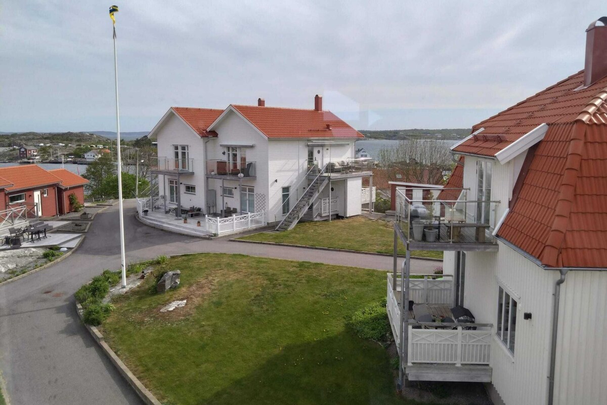 A two-story white building with a red roof, a flagpole, and a small deck with outdoor furniture.
