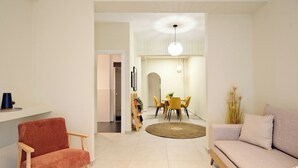 Een moderne woonkamer met een bank, een rode fauteuil, een eethoek met een tafel en stoelen, en een keuken op de achtergrond.