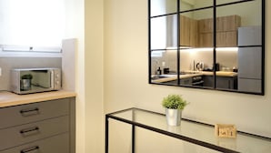Een moderne keuken met een magnetron, een glazen tafel met een plant, en een lijst met spiegel die de keuken weerspiegelt.