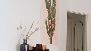 Een moderne, minimalistische kamer met een witte en houten console tafel, een kunstwerk met een cactusschilderij en een spiegel.