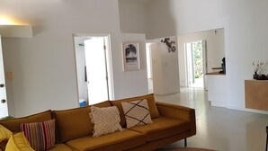 Een moderne woonkamer met een bank, een eethoek en een keuken, zichtbaar door een open deur.