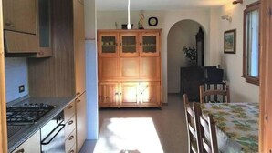 Et kompakt køkken med træskabe, en gasblus og et spiseområde med et bord og stole.
