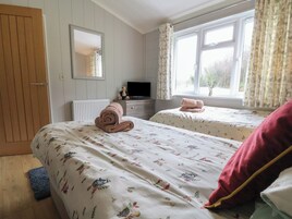 Un dormitorio con dos camas, un aparador, un televisor y una ventana con cortinas.