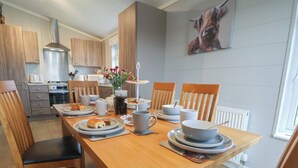 A modern kitchen with wooden cabinets, a stainless steel range hood, and a dining area with a wooden table set for four. - Holly Lodge (Holywell)