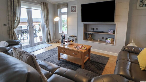 A modern living room with a sofa, coffee table, and TV. - Holly Lodge (Holywell)