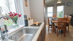 A modern kitchen with a stainless steel sink, wooden cabinets, and a dining area with a table and chairs. - Holly Lodge (Holywell)
