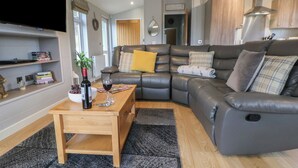 A modern living room with a leather sofa, a wooden coffee table, and a flat-screen TV. - Holly Lodge (Holywell)