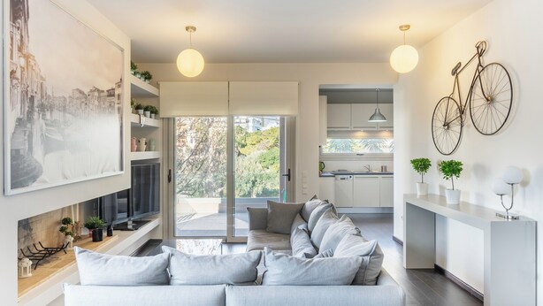 A modern living room with a sofa, a large painting, and a kitchen in the background. - New 2 Bedrooms, 2 Bath Apt in Central Glyfada, Fast WiFi, 10Min Walk to Beach (Glyfada)