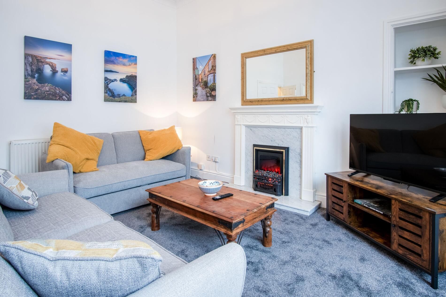 Una sala de estar con sofá, mesa de centro, chimenea, televisor y obras de arte en la pared.
