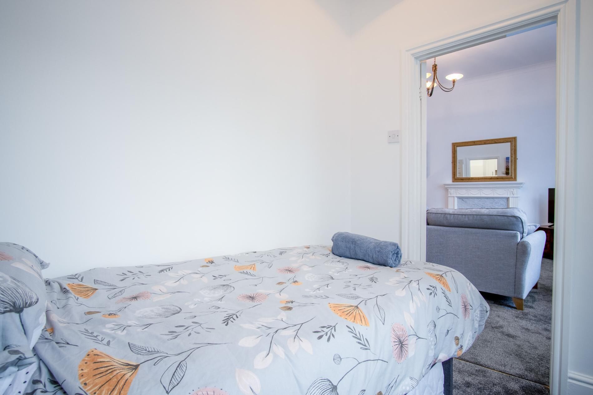Een slaapkamer met een bed, een grijze bank en een spiegel aan de muur.